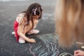 A cute little girl and mother drawing with colorful chalks on the playground. Child playing with her mom the summer`s games Royalty Free Stock Photo