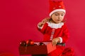 A cute little girl in a New Year`s costume throws Christmas decorations on a red background and space