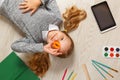 Cute little girl with O letter lying on the floor. The child is surrounded by a book, tablet, paints, brushes, pencils Royalty Free Stock Photo