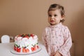 Cute little girl one and a hulf year old stand by delicious birthday cake. Eighteen month old girl verry happy and Royalty Free Stock Photo