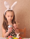 Little girl painting easter eggs at home.