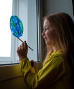 Cute little girl painting planet on window at home. Happy Earth Day April 22 greeting message.Creative family leisure