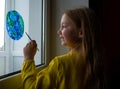 Cute little girl painting planet on window at home 4K. Happy Earth Day April 22 greeting message.Creative family leisure