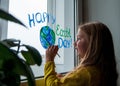 Cute little girl painting planet on window at home 4K. Happy Earth Day April 22 greeting message.Creative family leisure