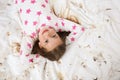 Cute little girl in pajamas lying among feathers on bed, top view. Happy childhood Royalty Free Stock Photo