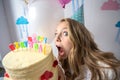 cute little girl in party cap biting birthday cake and looking Royalty Free Stock Photo