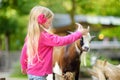 Cute little girl petting and feeding a goat at petting zoo. Child playing with a farm animal on sunny summer day. Royalty Free Stock Photo