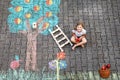 Cute little girl picking apples from apple tree painted with colorful chalks on asphalt. Cute preschool child with Royalty Free Stock Photo