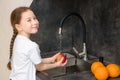 cute little girl with pigtail is happy to wash fruits in the kitchen - apples and oranges - and smiles Royalty Free Stock Photo