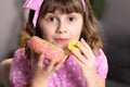 Cute little girl in pink dress holding macaron and donut in hands by the face. Funny concept with sweets. Adolescent