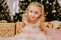 Cute little girl in pink dress with present on background Christmas tree Royalty Free Stock Photo