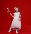 Cute little girl in a pink fairy costume with wings and a magic wand on a red background. Royalty Free Stock Photo