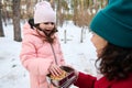 Cute little girl in pink pastel warm winter clothes takes a cookie out of a lunch box and enjoys a break for lunck with her loving Royalty Free Stock Photo