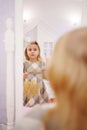 a cute little girl in a plaid dress looks in the mirror and primping.