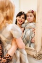 a cute little girl in a plaid dress and mom looks in the mirror and primping. Royalty Free Stock Photo