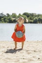 Cute little girl in a red dress plays with a ball on the sand Royalty Free Stock Photo