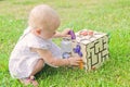 Cute little girl is playing with busiboard outdoors on green grass. Educational toy for toddlers. girl opened door to cube of Royalty Free Stock Photo