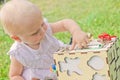 Cute little girl is playing with busiboard outdoors on green grass. Educational toy for toddlers. girl opened door to cube of Royalty Free Stock Photo