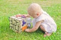 Cute little girl is playing with busiboard outdoors on green grass. Educational toy for toddlers. girl opened door to cube of Royalty Free Stock Photo