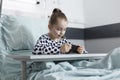 Cute little girl playing games on smartphone while resting on bed in pediatric hospital room. Royalty Free Stock Photo