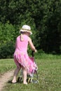 Cute little girl playing with her baby carriage on the meadow on sunny summer day.