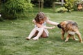 A cute little girl is playing with her pet dog outdooors on grass at home