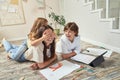 Cute little girl playing with mother and having fun while lying together on the floor at home, brother looking at them Royalty Free Stock Photo