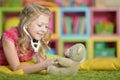 Cute little girl playing nurse, inspecting teddy bear with stethoscope