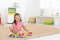 Cute little girl playing with toys on floor at home, space for text Royalty Free Stock Photo