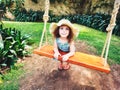 Cute little girl playing on a wooden swing wearing a big summer hat Royalty Free Stock Photo