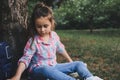 Cute little girl with ponytails, dressed in checkered shirt and blue jeans, relaxing in the park, sitting on green grass Royalty Free Stock Photo