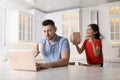 Cute little girl popping paper bag behind father`s back while he working at home