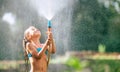 Cute little girl pours herself from the hose, makes a rain. Hot