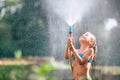 Cute little girl pours herself from the hose, makes a rain. Hot