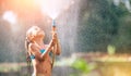 Cute little girl pours herself from the hose, makes a rain. Hot summer day pleasure
