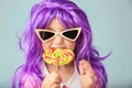 Cute little girl in purple wig eating lollipop on color background Royalty Free Stock Photo