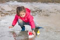 Cute little girl in rain boots playing with colorful ships in the spring creek standing in water Royalty Free Stock Photo