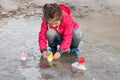 Cute little girl in rain boots playing with ships in the spring water puddle Royalty Free Stock Photo