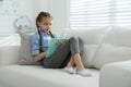 Cute little girl reading book on sofa at home Royalty Free Stock Photo