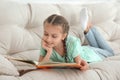 Cute little girl reading book on sofa at home Royalty Free Stock Photo