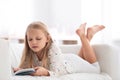 Cute little girl reading book on sofa at home Royalty Free Stock Photo