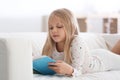 Cute little girl reading book on sofa at home Royalty Free Stock Photo