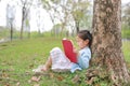 Cute little girl reading book in summer park outdoor lean against tree trunk in the summer garden Royalty Free Stock Photo