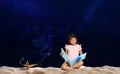 Cute girl reading magic book and Aladdin magic lamp on sand at night Royalty Free Stock Photo