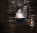 Cute little girl reading on floor in room full of stacked books Royalty Free Stock Photo