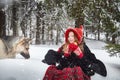 Cute little girl in red cap or hat and black coat with basket of green fir branches treats with a pie of big dog