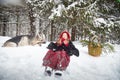 Cute little girl in red cap or hat and black coat with basket of green fir branches treats with a pie of big dog