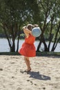 Cute little girl in a red dress plays with a ball on the sand Royalty Free Stock Photo