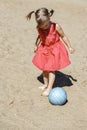 Cute little girl in a red dress plays with a ball on the sand Royalty Free Stock Photo