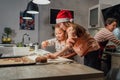 Cute little girl in red Santa hat with mother making homemade Christmas gingerbread cookies using cookie cutters together in home Royalty Free Stock Photo